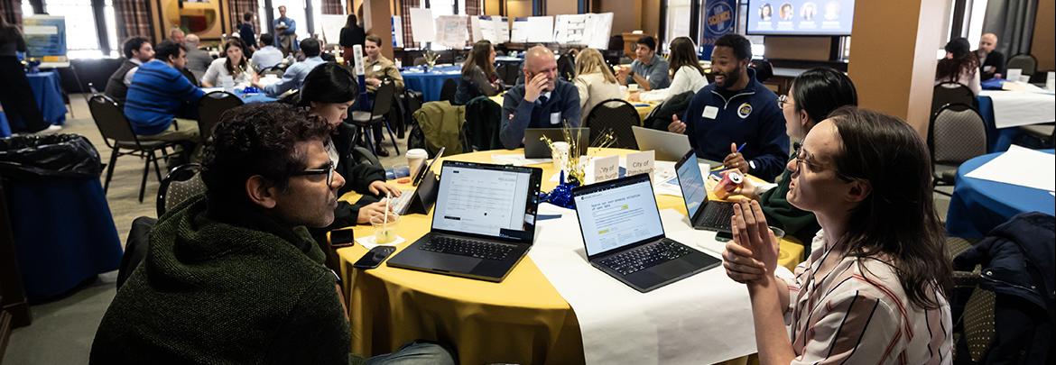 Data Science Day attendees gather around a round table with their laptops to discuss conference topics during breakout session.