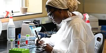 student taking notes among vials and solutions in research lab.