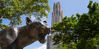 Panther statue with Cathedral of Leraning and leafy green trees in background.