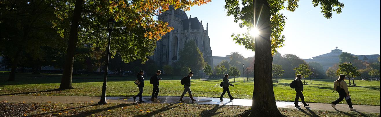 Sillhouettes of students walking across Cathedral lawn on a dewy fall morning.